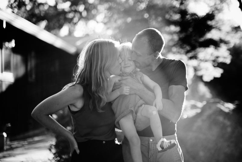 Parents kissing their toddler in low backlight, black and white