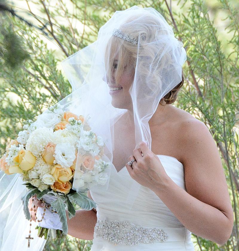 Bride smiling beneath a sheer veil, holding peach and ivory roses