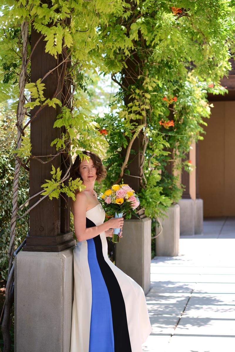 Bride in a colour-block gown leaning on a vine-covered pergola column
