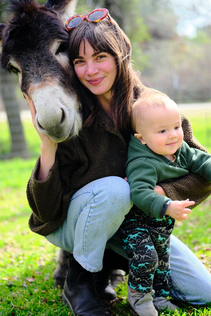 Mother cheek to cheek with a donkey, holding her smiling baby