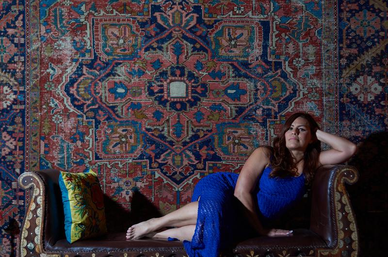Woman in a cobalt dress reclining before a faded Persian rug