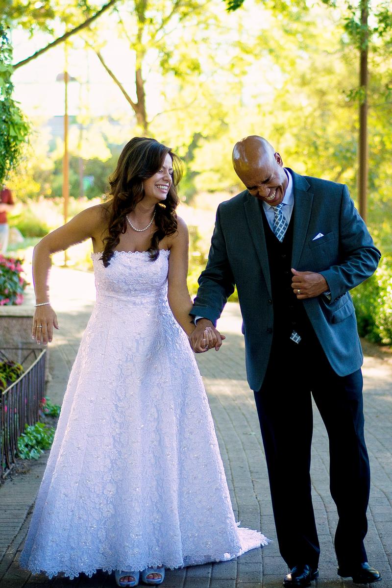 Bride and groom laughing as they walk hand in hand along a garden path