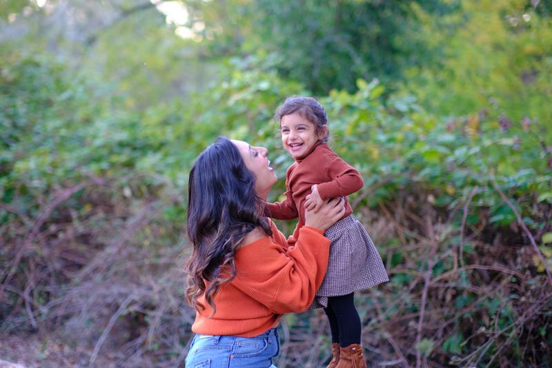 Mother lifting her laughing daughter against green woodland