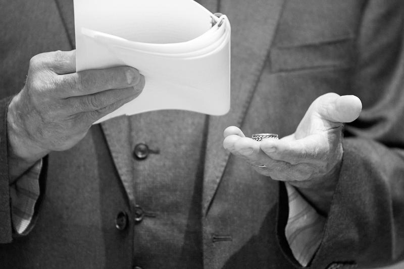 Officiant's open palm holding a wedding band beside the vows, black and white