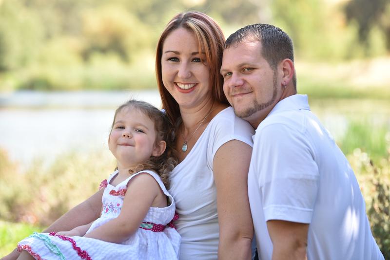 Mother, father and their young daughter smiling together by the water
