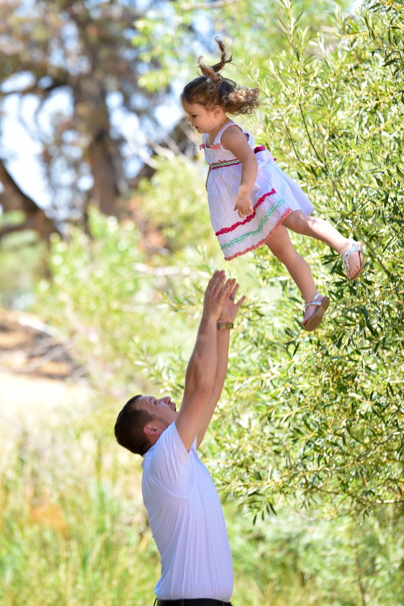 Father tossing his young daughter into the air beside an olive tree